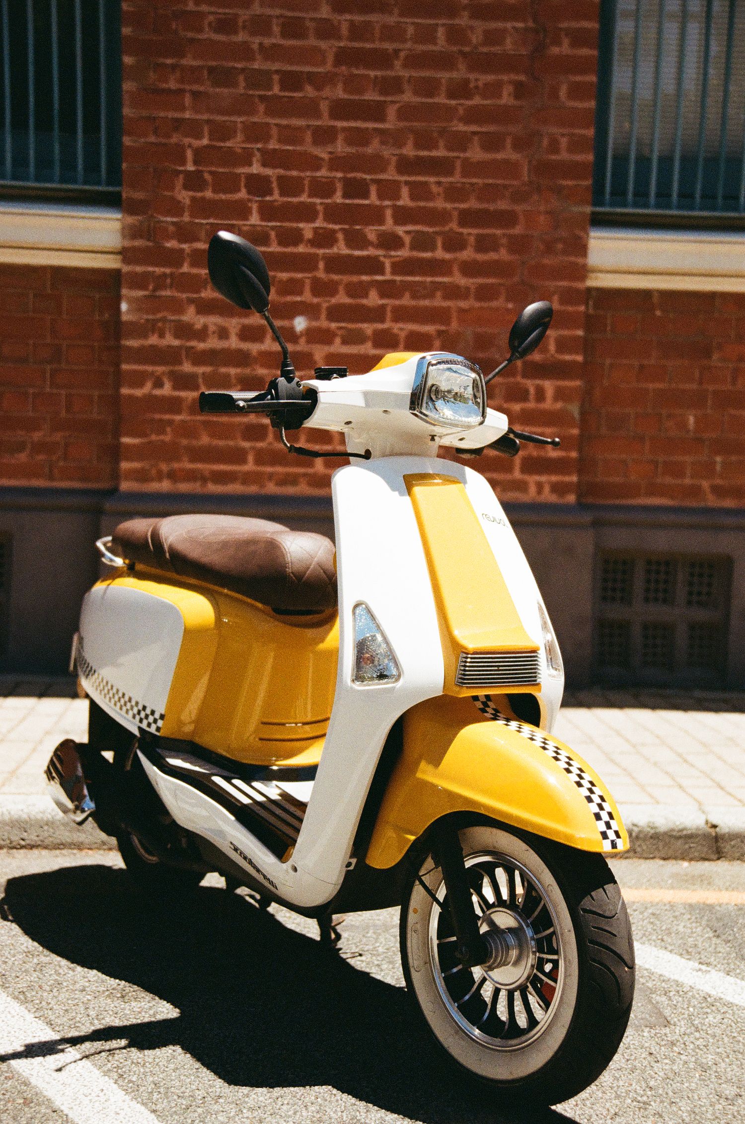 Yellow and white retro scooter parked against brick wall in sunlight.