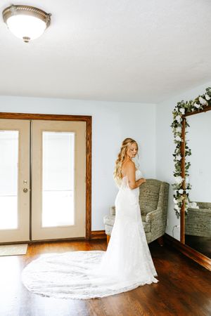 A flowing white wedding dress with a long train twirls elegantly across a hardwood floor in an empty room.