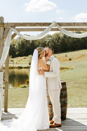 A romantic couple shares a tender moment on a wooden deck overlooking a scenic lake and rolling hills.