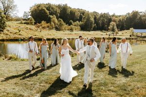 Wedding party in white attire walking together across a sunlit grassy field.