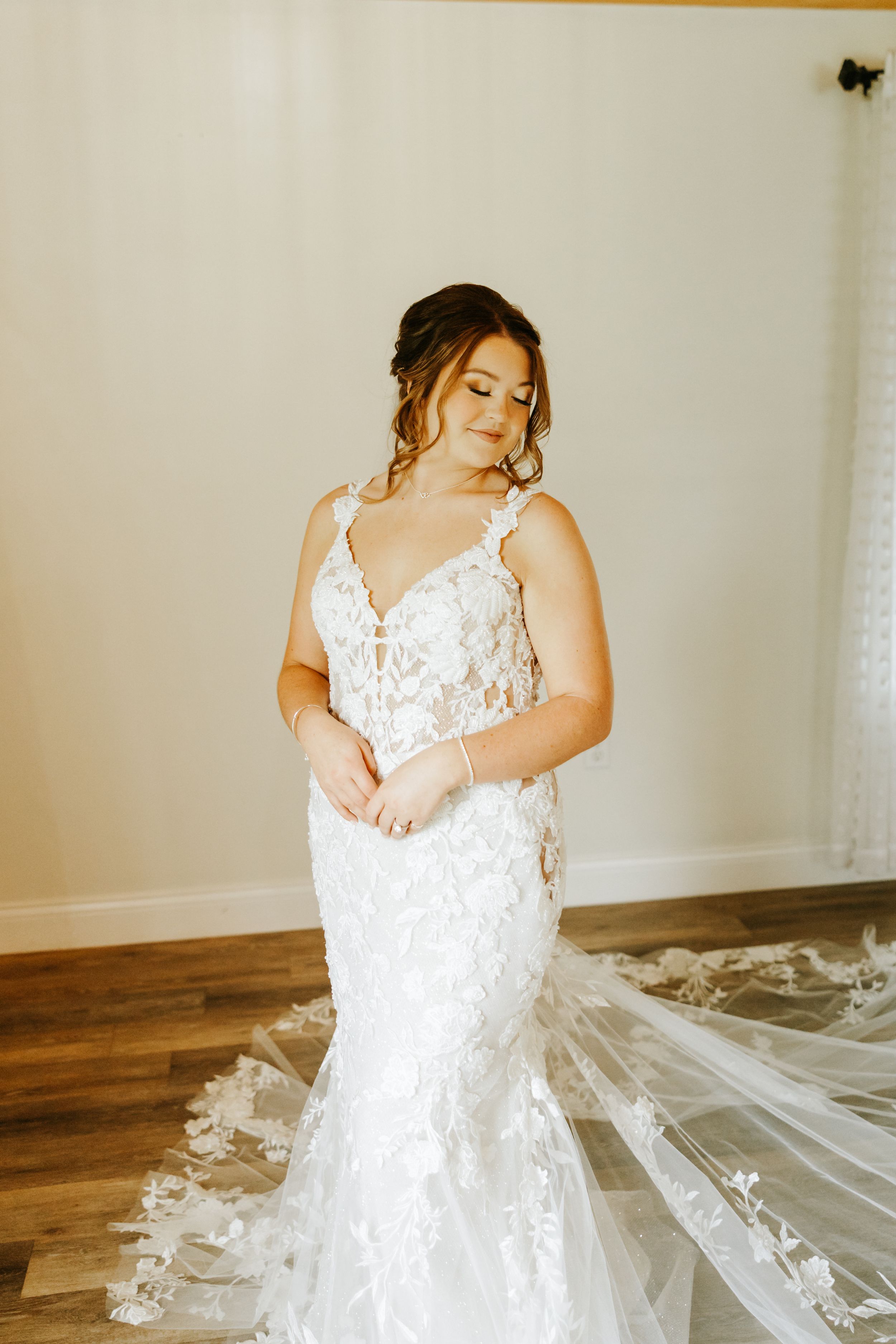 A flowing white lace wedding dress with intricate floral details spreads elegantly across a wooden floor.