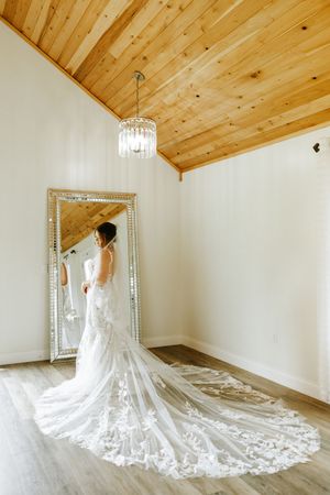 A stunning white lace wedding gown with a dramatic cathedral-length train displayed in a room with wood-paneled ceiling.