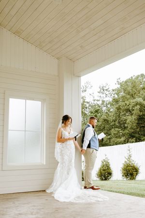Two people share an intimate first look moment on a white-painted porch before their wedding ceremony.