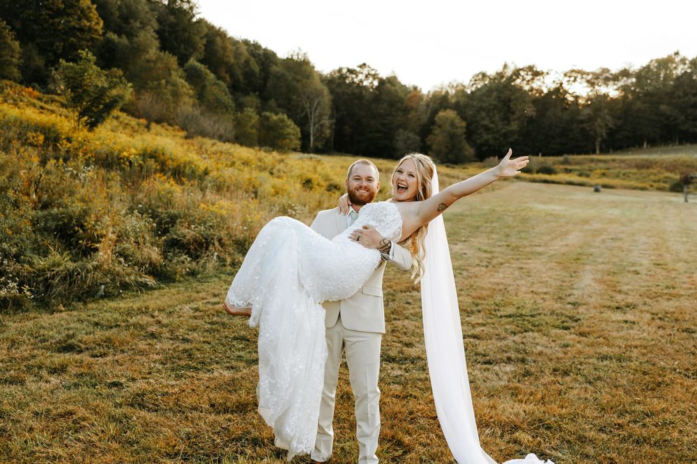 A couple in wedding attire dances together in a golden field at sunset during their outdoor celebration.