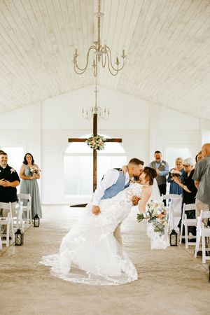 A romantic dip kiss during a wedding ceremony in a white chapel with guests watching.