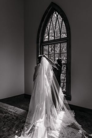 A series of black and white photos showing a flowing white wedding dress and veil against an arched church window.