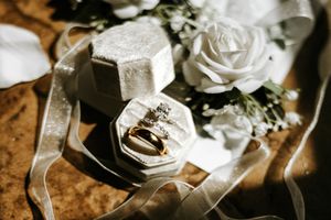 Wedding rings and wedding bands rest on a rustic wooden surface with scattered flower petals and soft lighting.