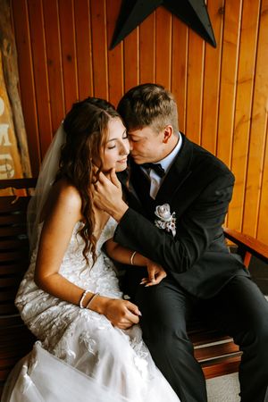 A romantic wedding photo series showing tender moments between newlyweds sitting on a wooden bench.