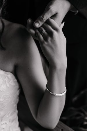 Close-up black and white photo of hands with bracelet against dark background.