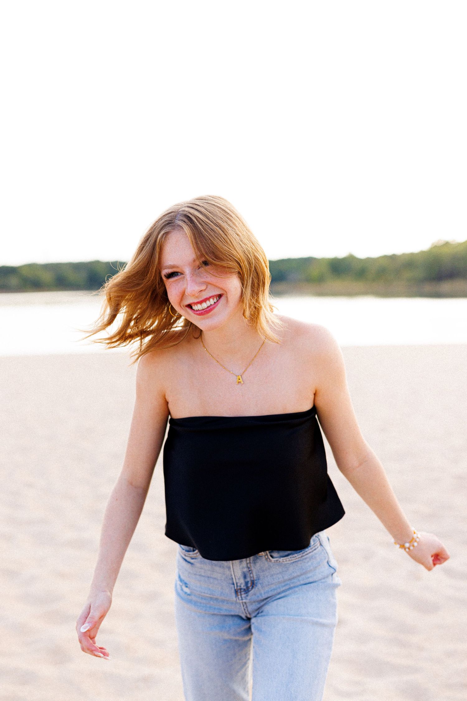 Joyful summer portrait on a beach wearing a black crop top and light denim against golden sunlight.