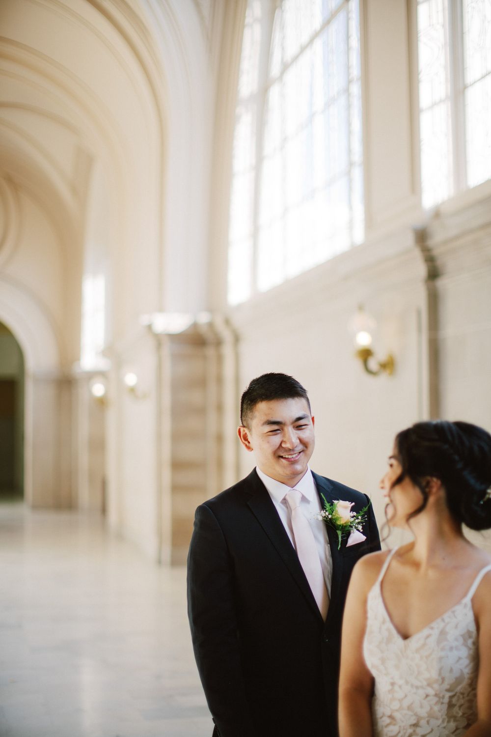 A wedding couple shares a joyful moment in an ornate white hallway.