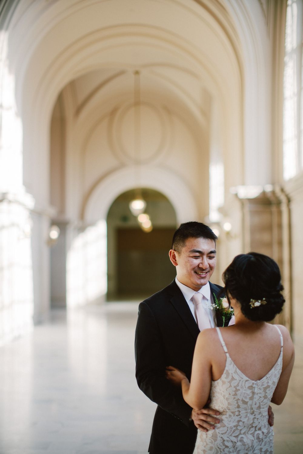A romantic wedding moment captured in a sunlit classical corridor.
