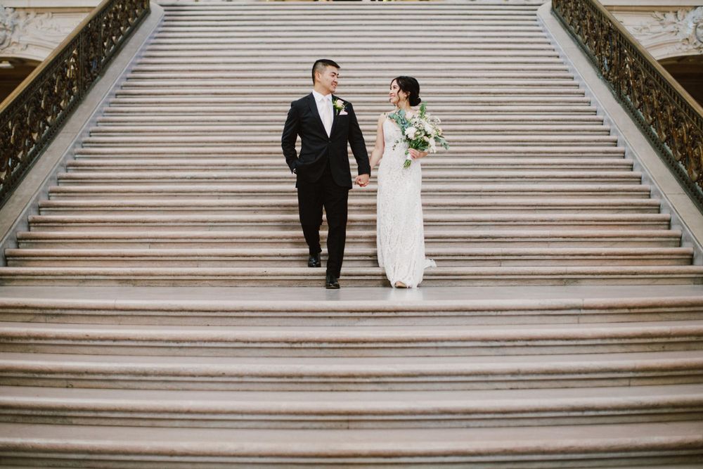 Couple descending elegant white marble staircase during wedding photoshoot.