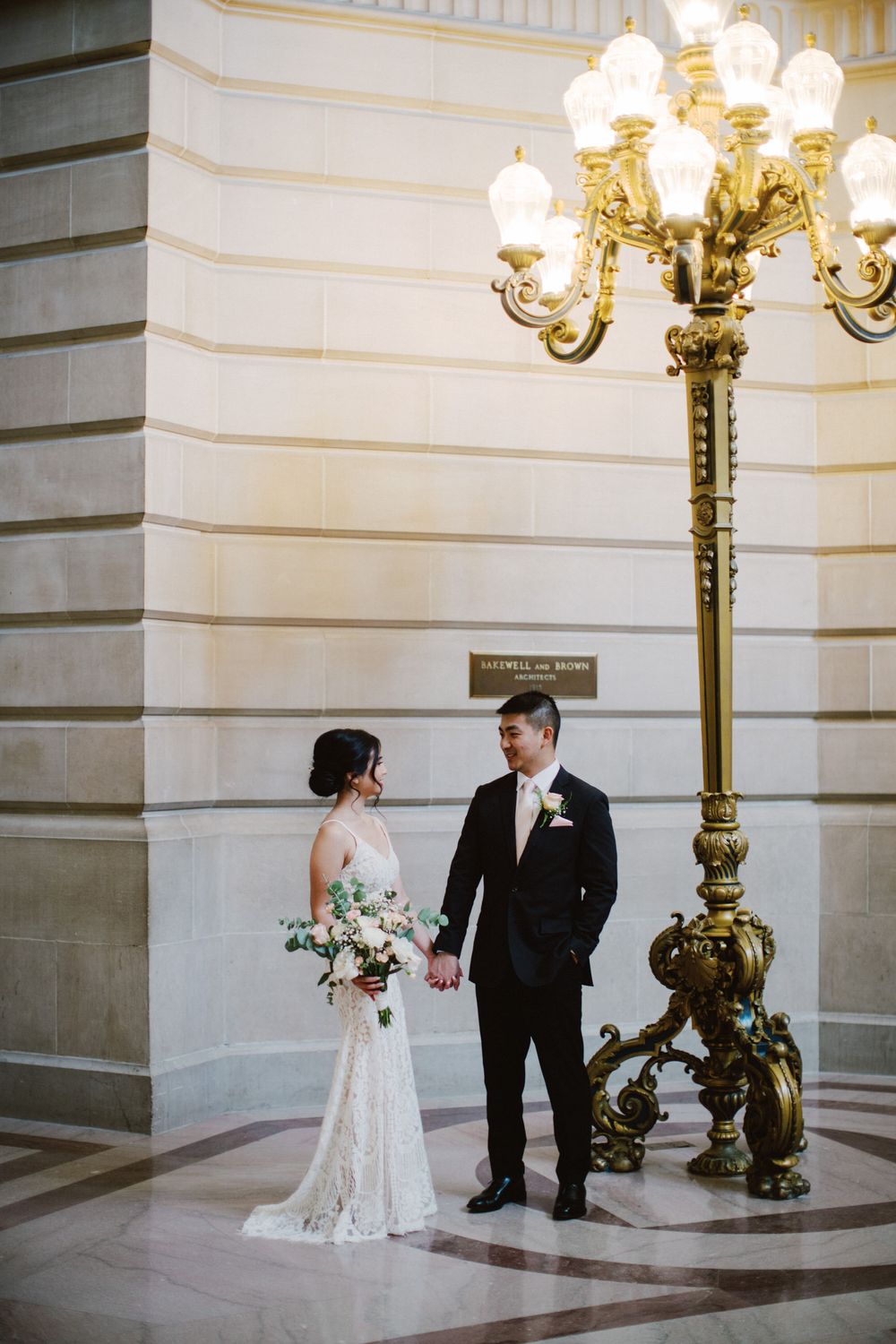 Romantic couple portrait by ornate vintage lamp post in classical building interior.