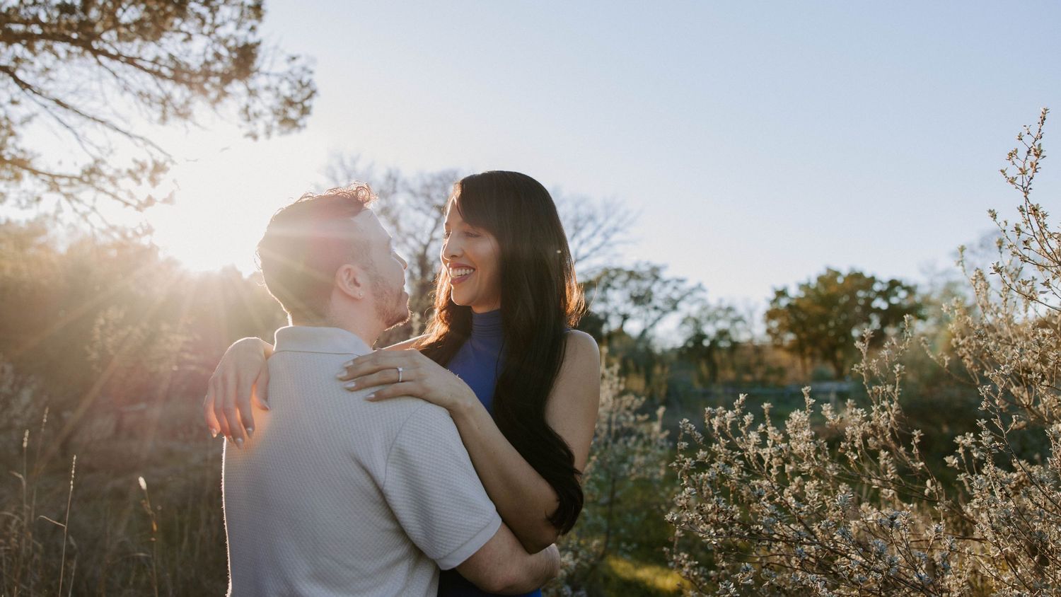 San Antonio Engagement Photography. Couple embracing in sunlit field during romantic outdoor photoshoot.