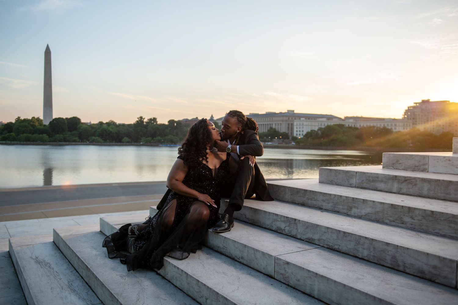 Couple sitting on stone steps at sunset with Washington Monument in background.