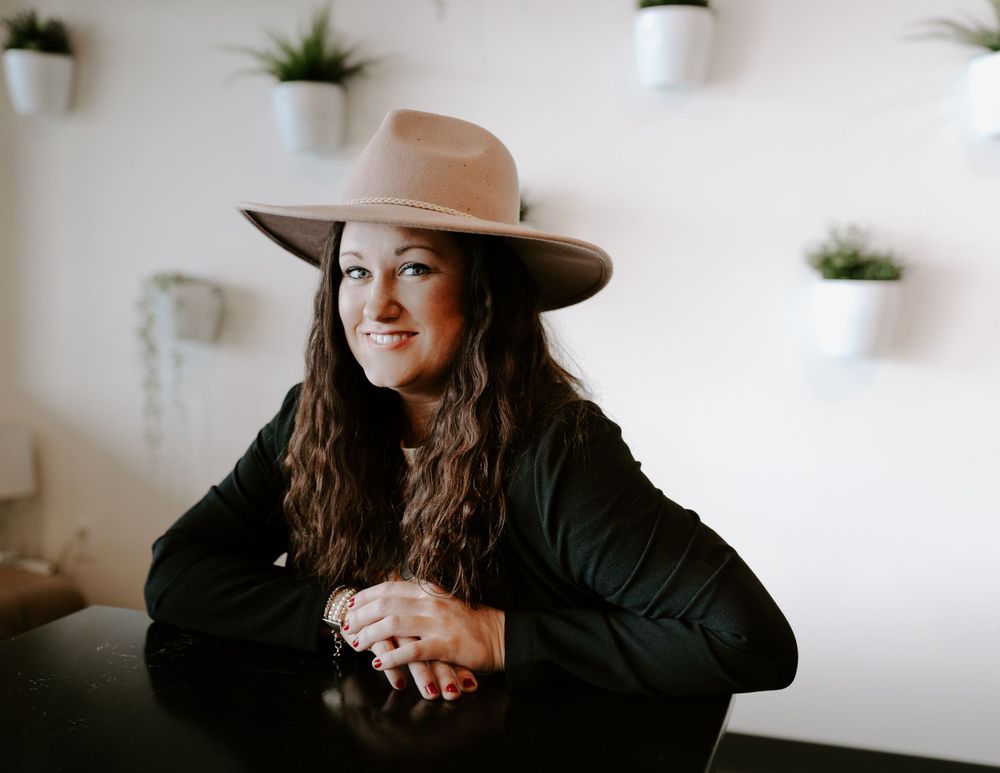 A person wearing a brown hat relaxes in a casual indoor setting with decorative plants on the wall.