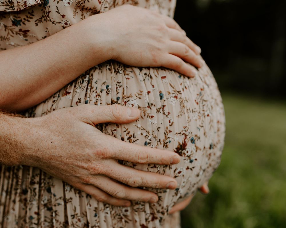 Close up of hands cradling a pregnant belly in a lace dress outdoors.