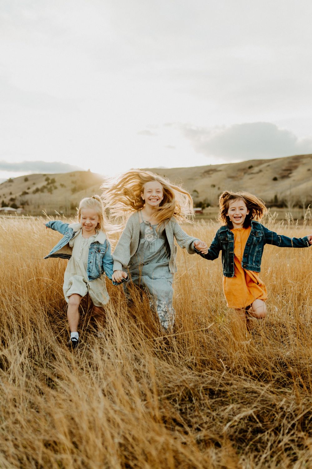 Three joyful children running and jumping through tall golden grass in field.