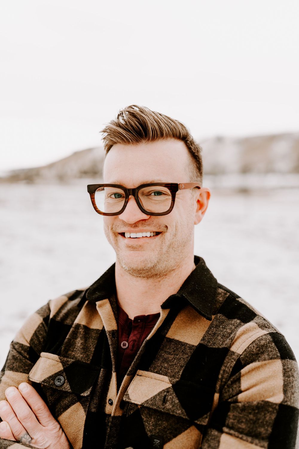 Portrait of a person in glasses and plaid flannel jacket smiling outdoors.