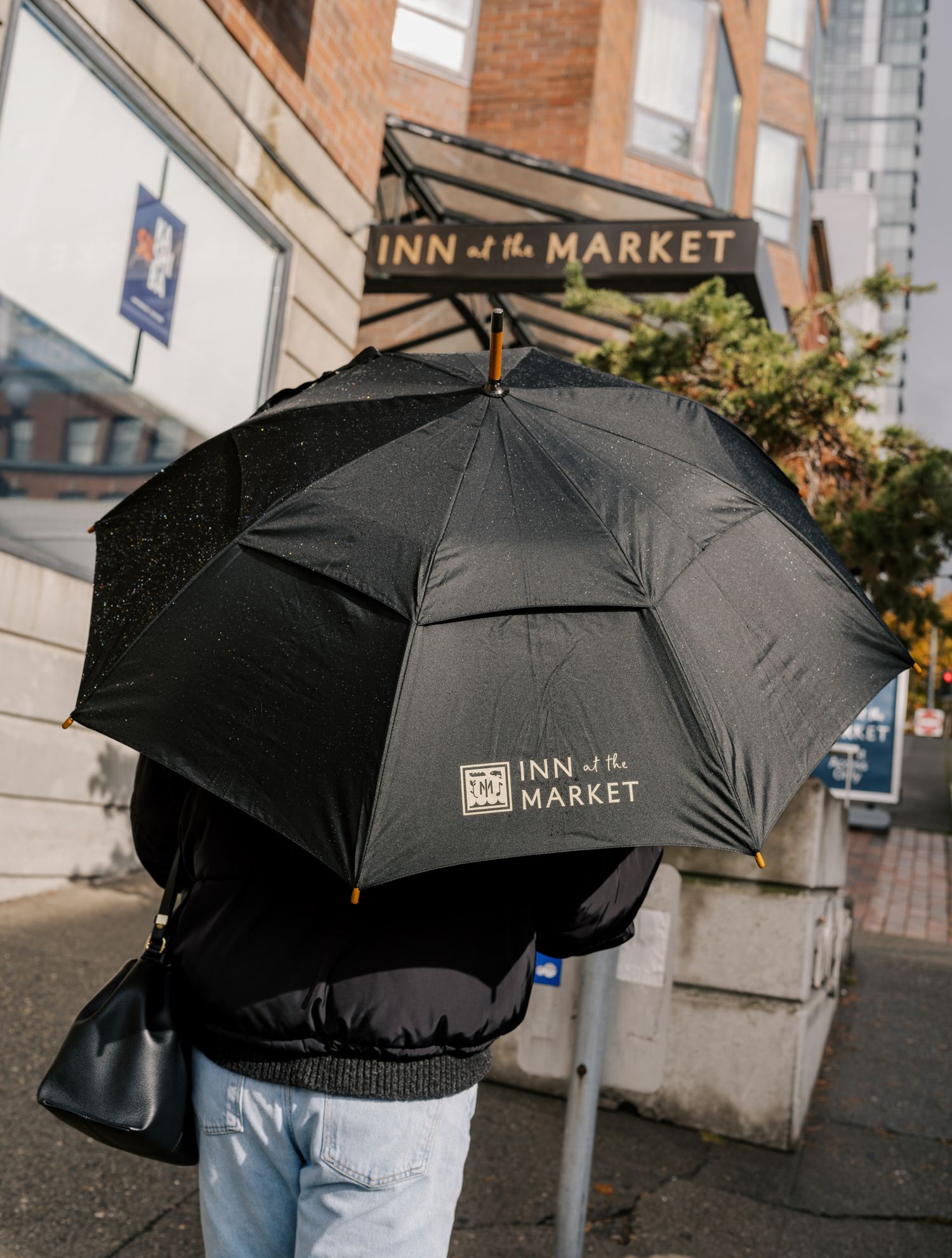 A black umbrella with Inn at the Market logo shown against a brick building storefront on a rainy day.
