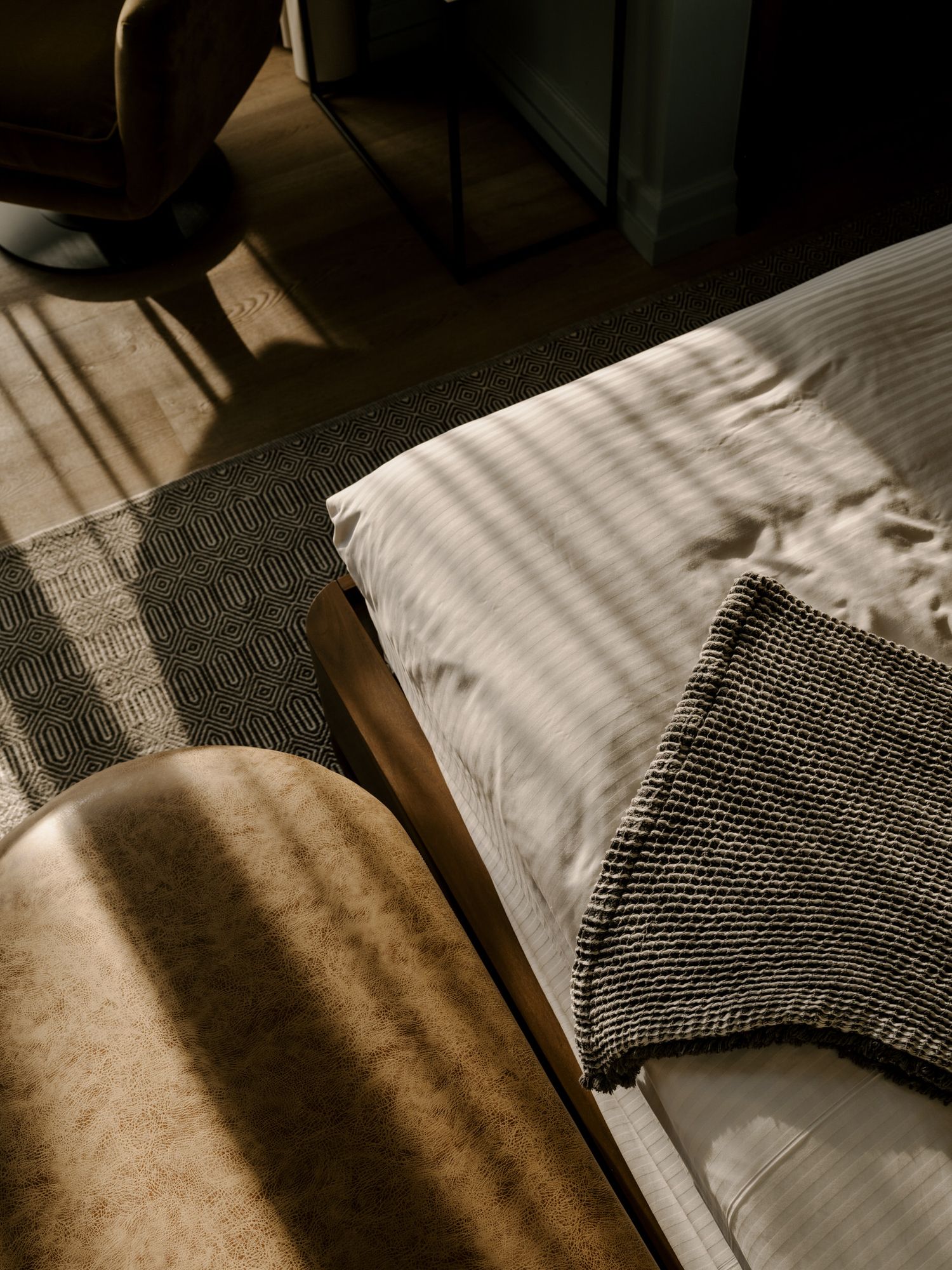 Sunlight casting dramatic shadows across a bed with white striped bedding and textured gray throw blankets.