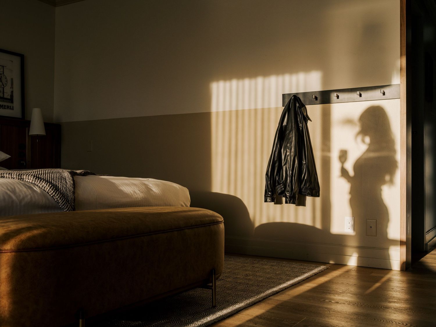 A silhouette stands in a doorway casting shadows across a modern living room with a couch in warm afternoon light.