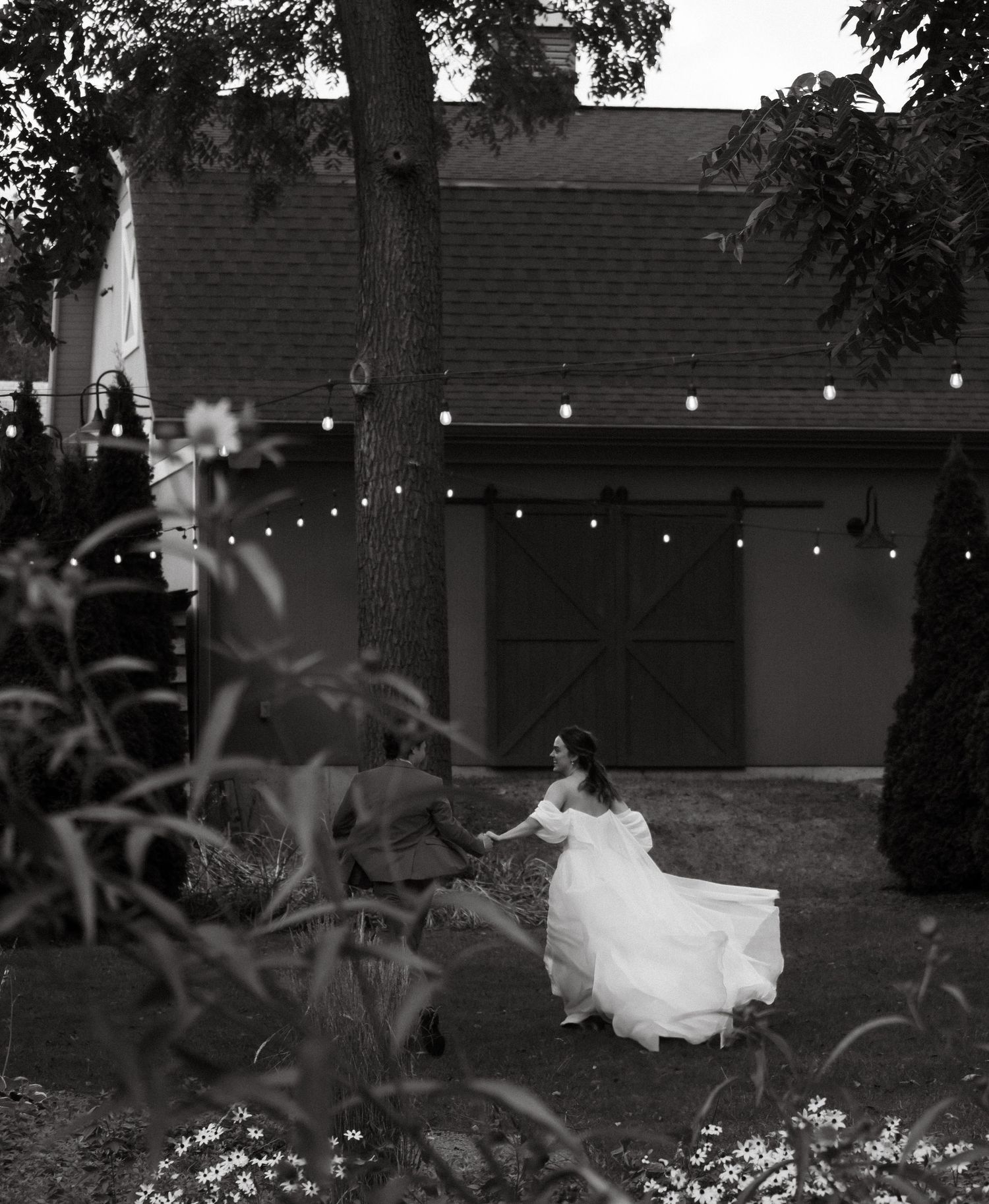 A bride in a flowing white dress twirls under string lights at dusk.