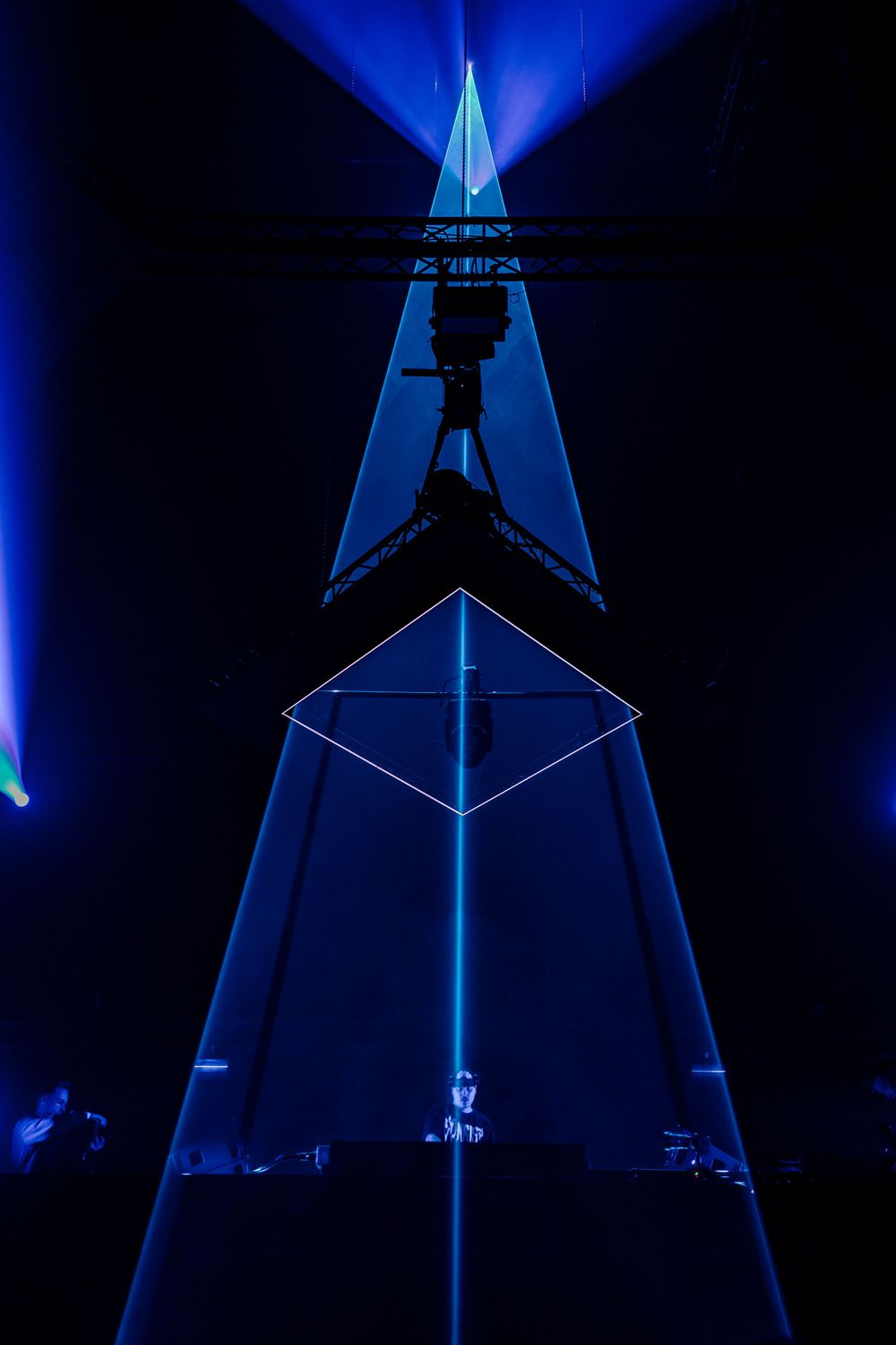 Triangular stage structure illuminated by blue lighting creates geometric patterns against dark background.