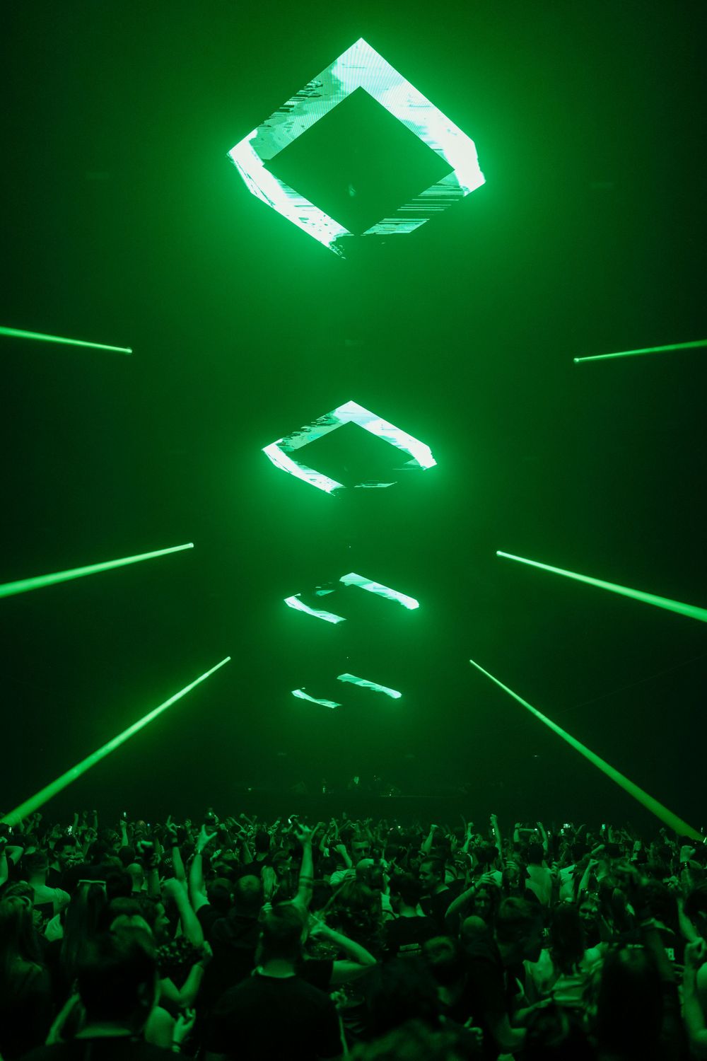 Geometric green lighting installations hover above a packed concert crowd.