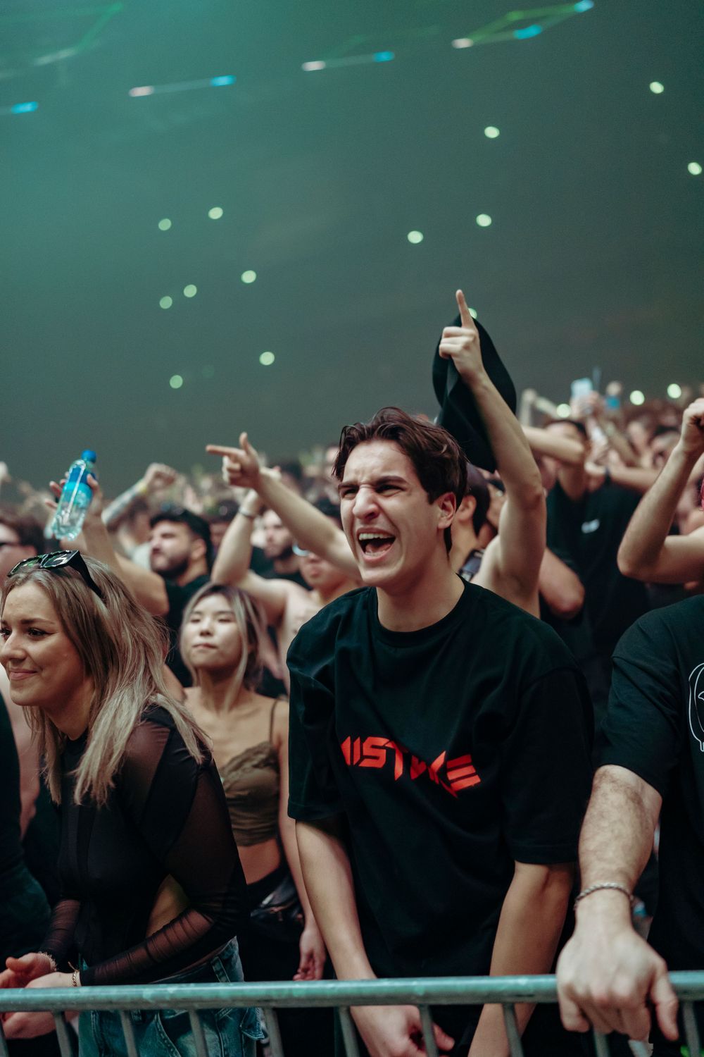 Excited crowd at an electronic music concert with hands raised under green lighting and spotlights.