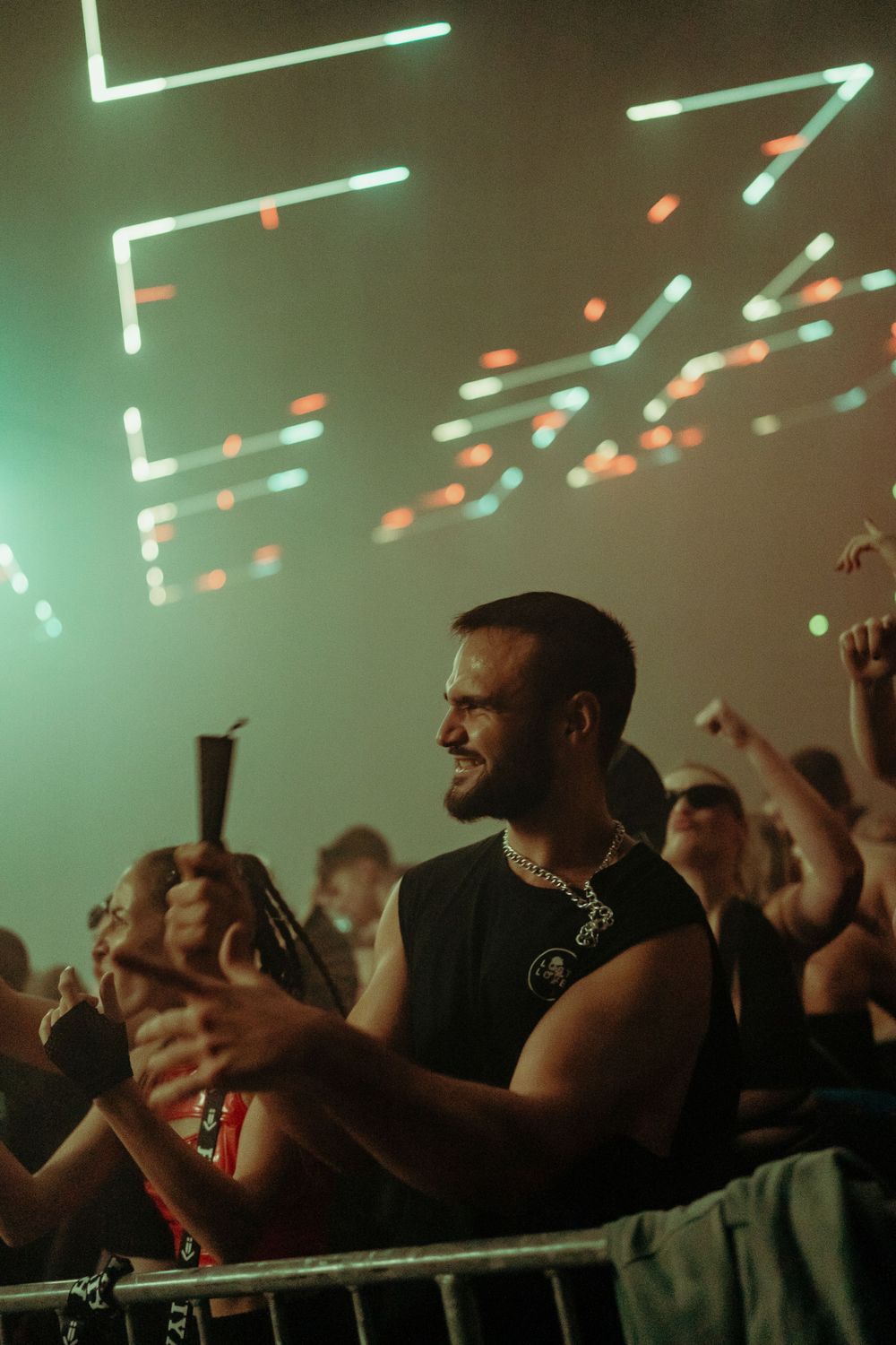 Concert attendees enjoying the show under geometric light patterns in green and orange hues.