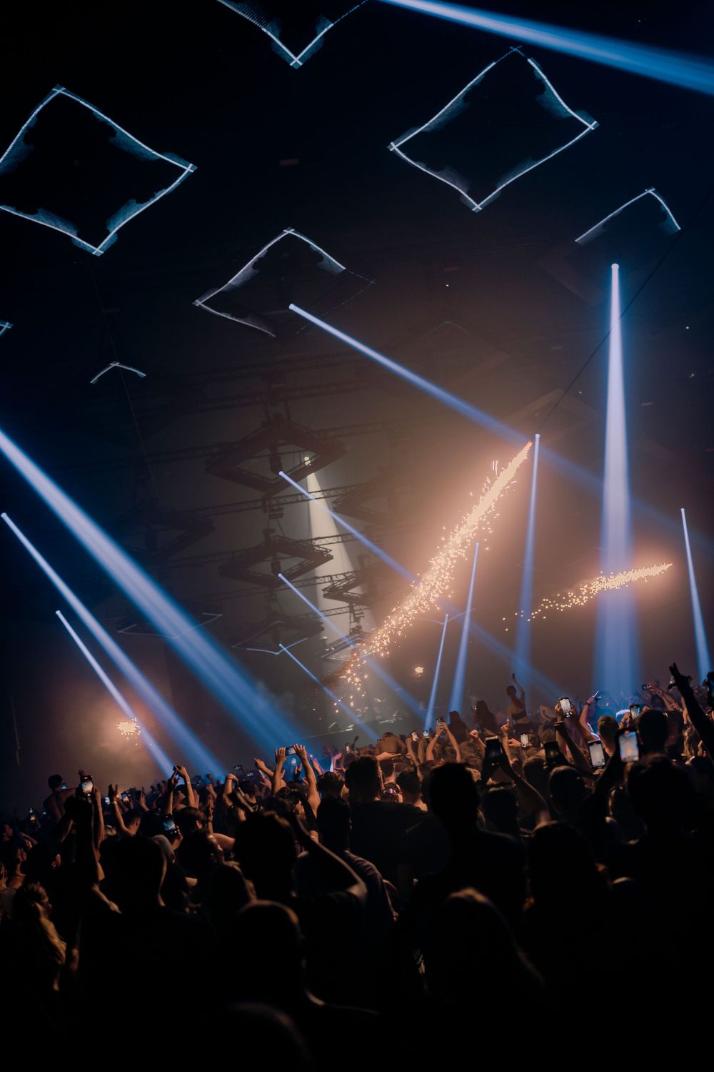Stunning light show with blue beams cutting through smoke above an energetic concert crowd.