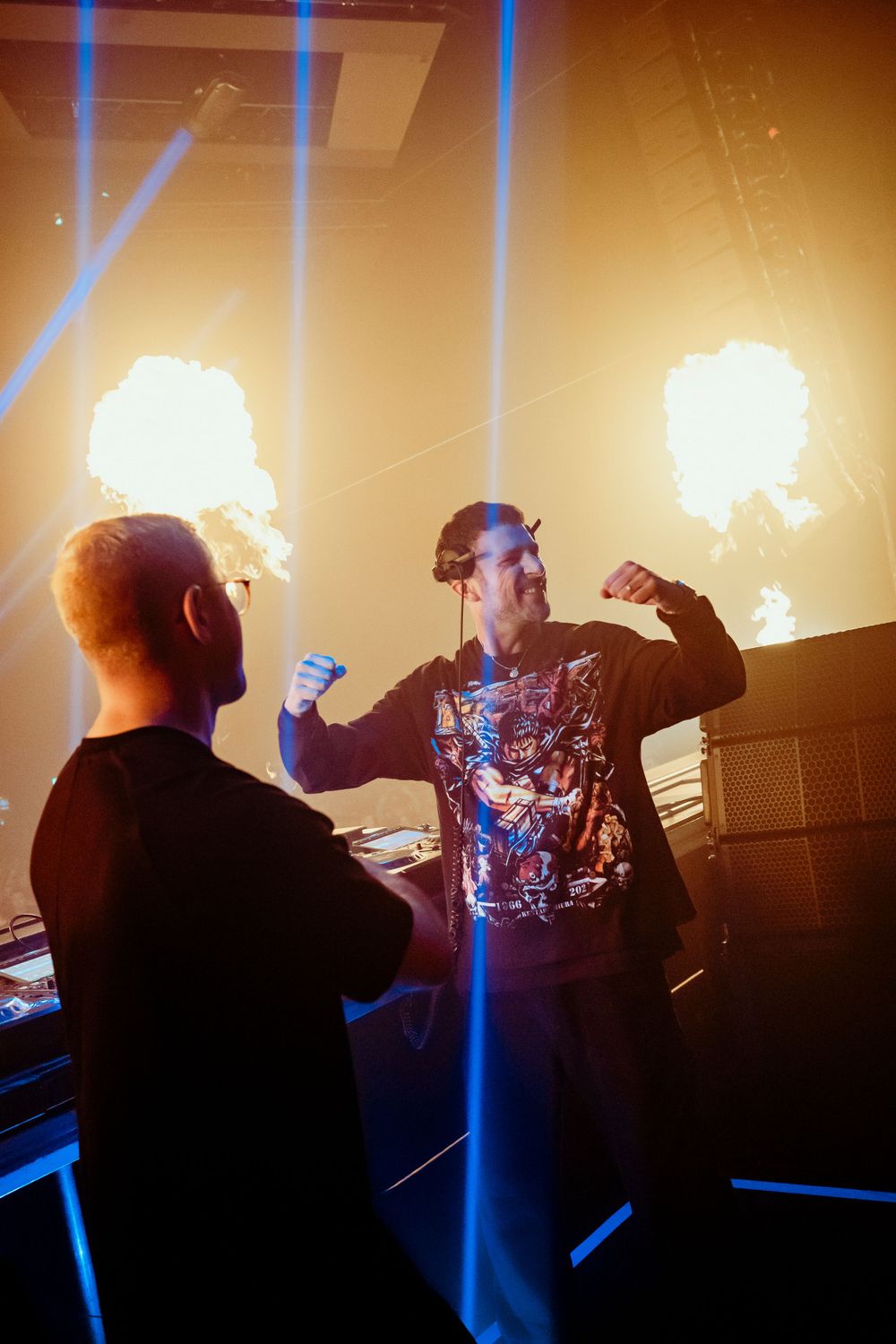 Performers silhouetted against dramatic blue light beams and orange stage lighting.