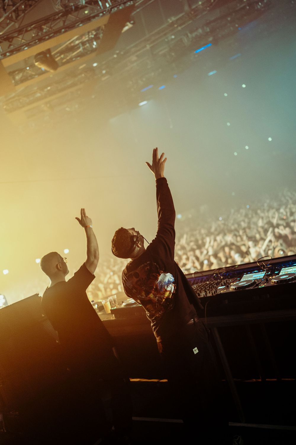 Concert crowd silhouettes against warm sunset lighting with hands raised in celebration.
