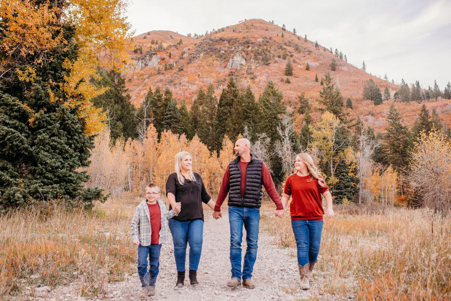 Family walking together on mountain trail surrounded by fall colors and evergreen trees.