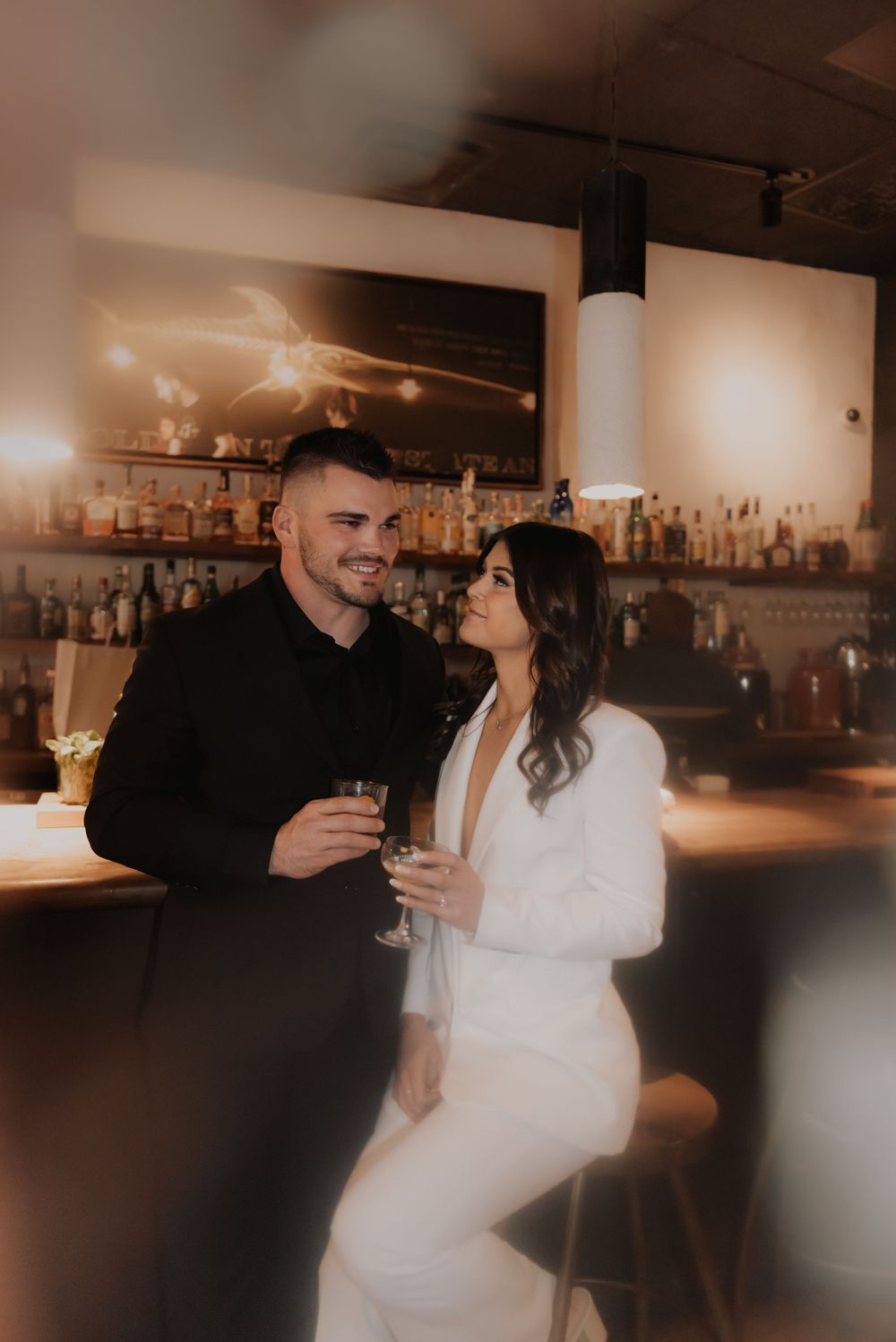 A stylish couple shares drinks at an upscale bar with ambient lighting.