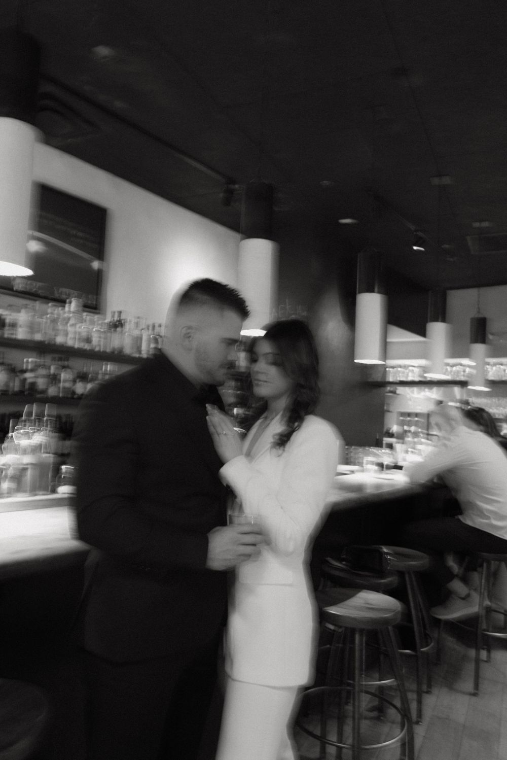 A motion-blurred black and white photo of a couple at a bar counter.