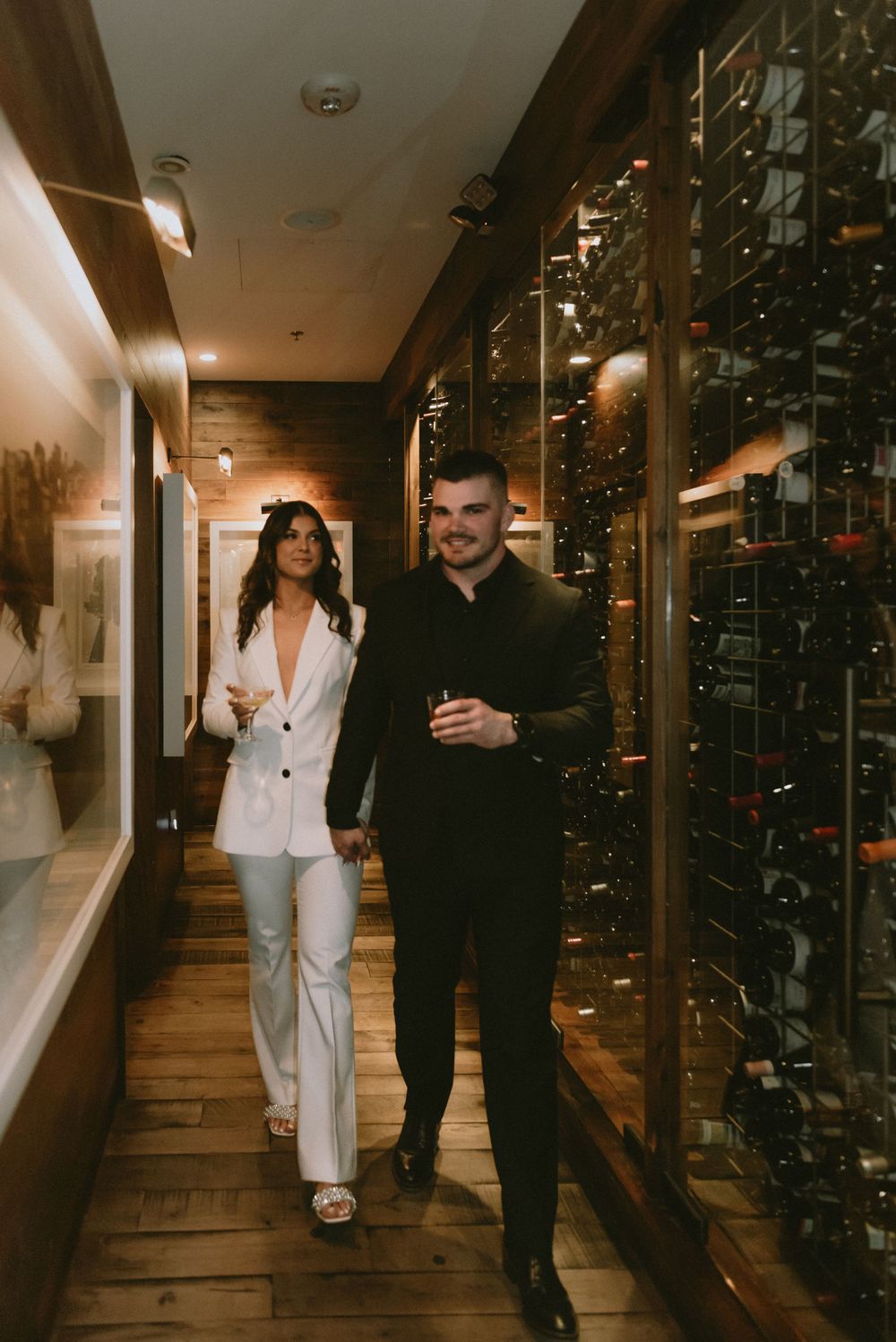 A couple walks through an elegant wine cellar with glass display walls.