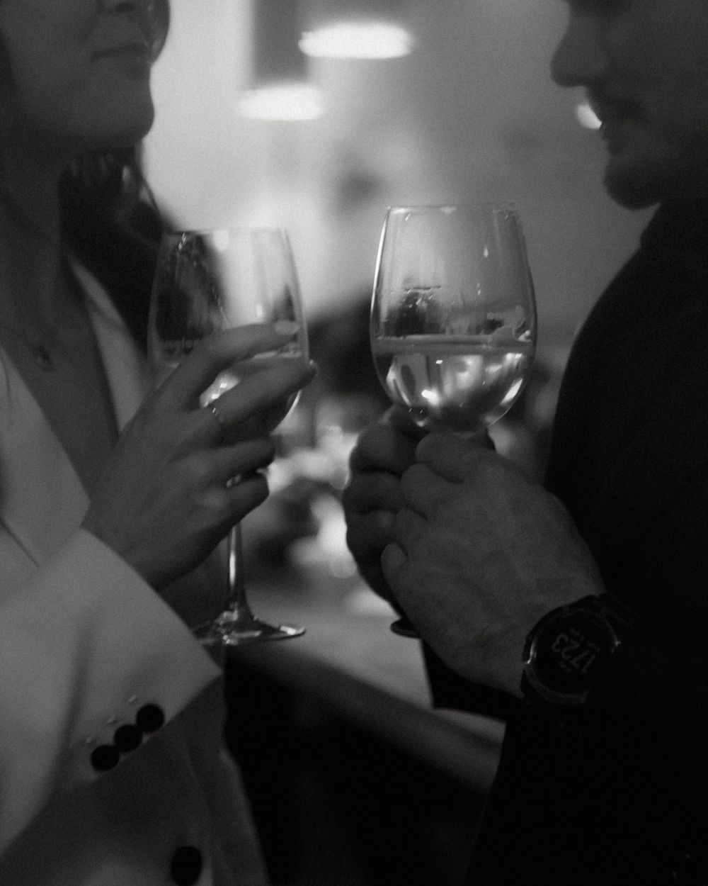 Two people share a romantic toast with wine glasses in black and white photography.