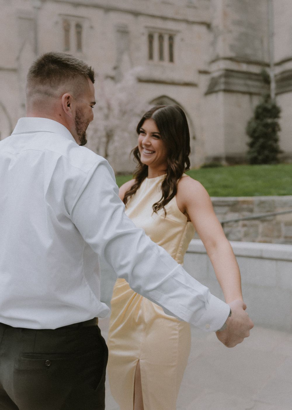 Dancing couple in formal attire share playful moment outside Gothic church architecture.