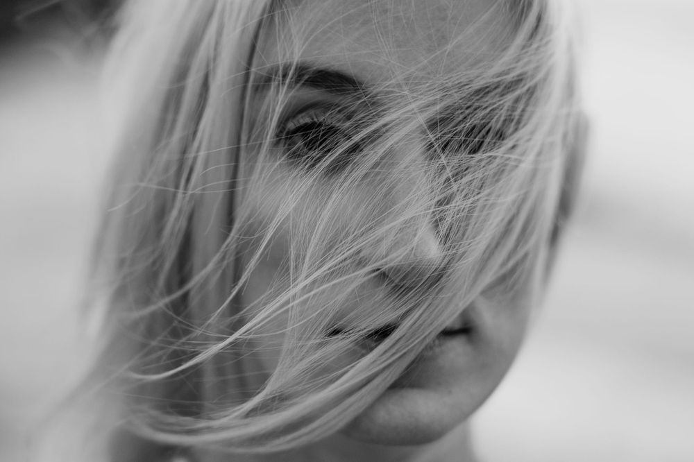 An artistic black and white close-up of windswept hair against a soft, blurred background.