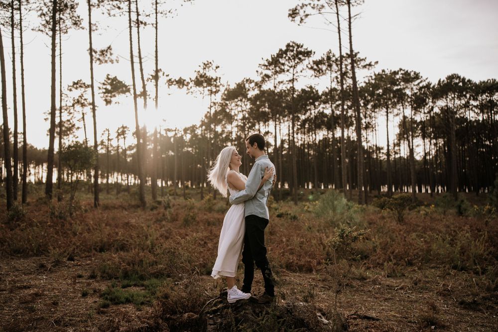 A romantic sunset embrace among tall pine trees in a rustic outdoor setting.