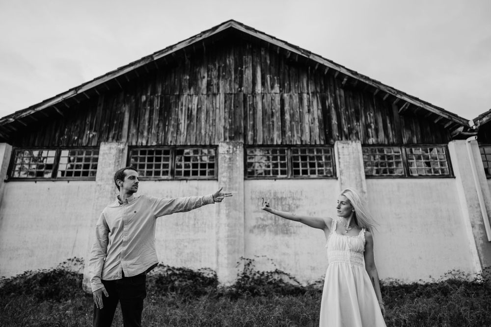 A couple strikes a whimsical pose with outstretched arms against an industrial backdrop.