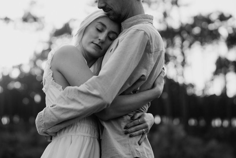 An intimate black and white portrait of a couple sharing a tender embrace outdoors.