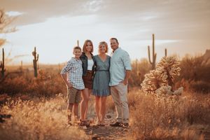 Family of four posing together in Arizona desert at sunset with saguaro cacti in warm golden light.
