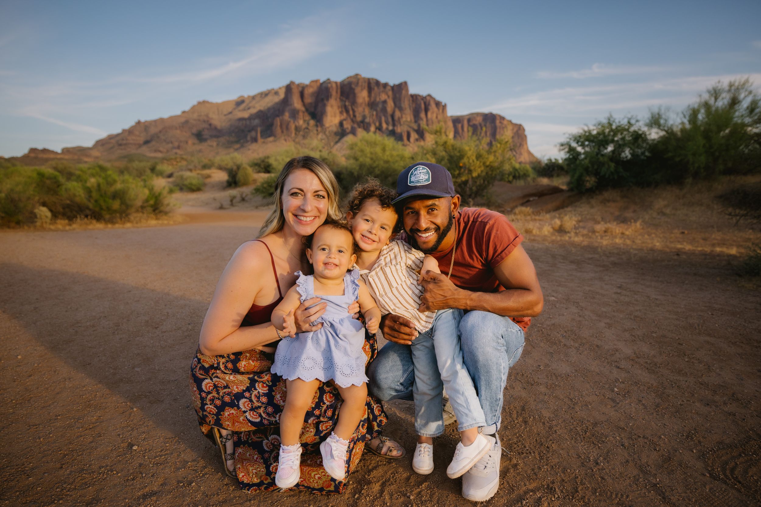 Family of four smiling together in the desert with Superstition Mountains in the background at golden hour.