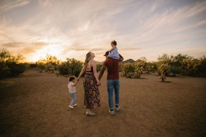 Family walking hand-in-hand at sunset in a desert landscape, with parents lifting children in a warm golden light.