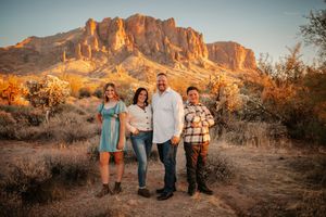 Family of four posing in Arizona desert with Superstition Mountains glowing at golden hour sunset behind them.
