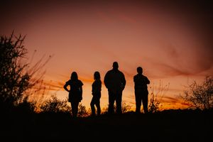 Silhouettes of four people standing against a vibrant orange and red sunset sky outdoors.